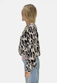 Bluzka w panterkę z długimi rękawami, wykonana z lekkiego materiału o luźnym kroju. Dolny brzeg wykończony różowo-białym ściągaczem. Noszona z dżinsami.