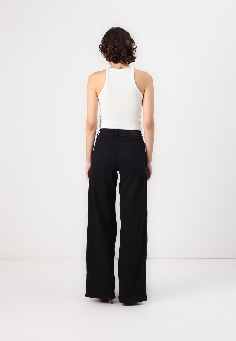 Pantalones de pierna ancha negros con cintura alta, hechos de un tejido resistente; combinados con una camiseta ajustada blanca. La parte trasera cuenta con dos bolsillos.