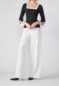 Haut noir avec un décolleté carré et des bordures blanches, associé à un pantalon blanc à jambes larges. Le haut présente des manches évasées et une coupe ajustée.