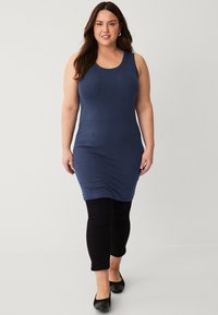 Donkerblauwe, mouwloze tankjurk met een aangesloten ontwerp, gecombineerd met zwarte leggings en platte schoenen. Gladde stof met een lichte rek.