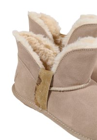Botas de tobillo de ante beige con un suave forro de piel de crema. Presentan un acento decorativo texturizado y detalles cosidos alrededor de los bordes.