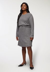 Vestito grigio a maglia con maniche lunghe, scollo rotondo e una cintura abbinata in vita. Indossato con scarpe slingback nere. Tessuto liscio.