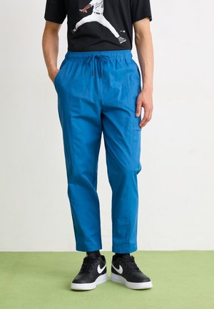 Male wearing blue drawstring pants, black Nike sneakers with white swoosh, and black T-shirt with a baseball player graphic.