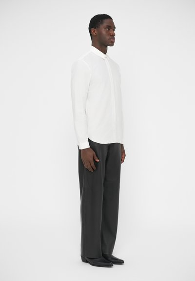Chemise blanche à manches longues avec un col structuré, associée à un pantalon noir à jambes larges et des chaussures noires. Tissu lisse, design minimaliste.