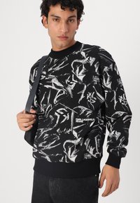 Black sweatshirt featuring a bold white abstract pattern, ribbed crew neck, and cuffs. Includes branding on the front left.