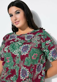 Burgunderfarbener kurzärmeliger Oberteil mit aufwendigen grünen, blauen und rosa Paisleymustern; runder Ausschnitt und weicher Stoffstruktur.