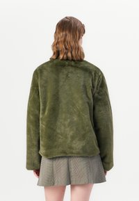 Zachte, olijfgroene faux fur jas met een relaxte pasvorm, voorzien van lange mouwen en een ronde kraag. Geassembleerd oppervlak met minimale detailering.