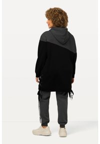 Schwarz- und grau farbblockierter Kapuzenpullover mit seitlichen Spitzenakzenten, kombiniert mit grauen Jogginghosen und hellen Sneakers. Strukturierter Stoff.