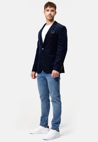 Marineblå kordfløjl blazer med reverslapeller, enkelt knaplukning og brystlomme. Parret med lyseblå jeans og hvide sneakers.