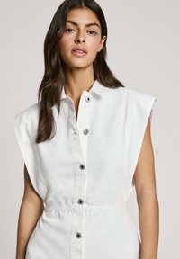 Witte denim jurk met korte, gestructureerde mouwen, een knoopsluiting aan de voorkant en een getailleerde taille. Bevat subtiele stikseldetails en metallic knopen.