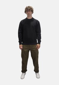 Felpa nera a girocollo con maniche lunghe abbinata a pantaloni cargo verde oliva. I pantaloni presentano più tasche e una vestibilità comoda. Le sneakers bianche completano l'outfit.