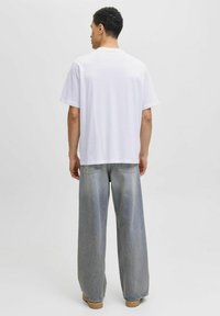 Weißes Baumwoll-T-Shirt mit kurzen Ärmeln, kombiniert mit hellgrauen, weit geschnittenen Jeans. Glatte Textur und lässige Passform von hinten präsentiert.