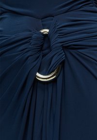 Tissu bleu marine rassemblé et torsadé à travers un anneau circulaire doré brillant, créant des plis drapés et de la texture.