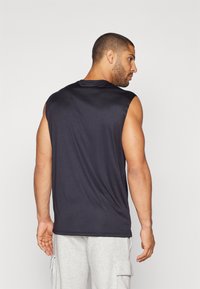 Camiseta atlética sin mangas de color navy con una textura suave y un drapeado sutil, con un escote redondo y un corte holgado, combinada con pantalones grises.