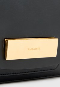 Borsa a mano in pelle nera con dettagli in metallo dorato e la scritta "ALLSAINTS" incisa. Texture liscia e forma rettangolare.