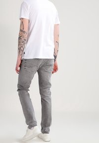 Grå denimjeans med slim fit, bakfickor med subtila sömmar, i kombination med en enkel vit t-shirt och vita sneakers.