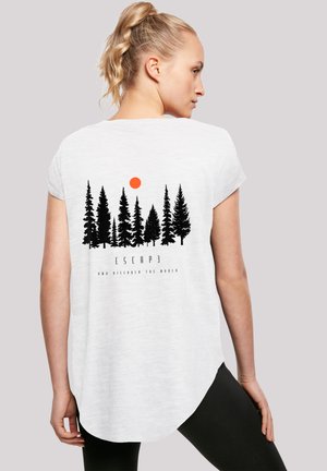Blonde woman with ponytail wearing white T-shirt featuring black pine trees and orange sun graphic with "ESCAPE AND DISCOVER THE WORLD" text.