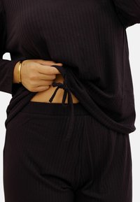 Ensemble de loungewear noir à côtes avec un cordon de serrage à la taille et une coupe décontractée. Matériau doux avec une surface texturée.