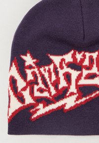 Ciemnofioletowa dziana czapka z czerwono-białym abstrakcyjnym wzorem geometrycznym w pobliżu dolnej krawędzi.