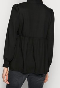 Blusa nera a maniche lunghe con vita arricciata, scollo rotondo e polsini elastici. Il tessuto liscio con una consistenza morbida mette in risalto il design minimalista.