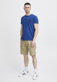 Blå bomull t-skjorte med en svart grafikk på brystet, kombinert med khaki cargo shorts. Avsluttet med hvite sneakers med svarte striper.