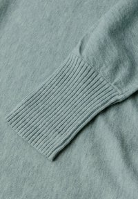 Manica di un maglione lavorato a maglia blu chiaro che presenta un polsino a costine e una consistenza morbida, evidenziando il tessuto liscio e una leggera variazione di colore.