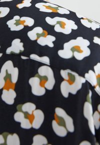 Button-up shirt with a black background, featuring a floral pattern in white, green, and orange. Smooth texture and casual design.