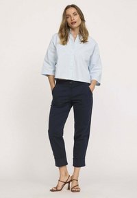 Chemise courte bleu clair à boutons et à manches 3/4, associée à un pantalon cropped navy et des talons brides marron. Texture lisse, design décontracté.