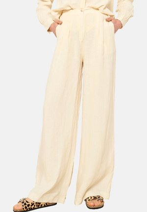 Linen wide-leg pants in light beige with pleats at the front, worn with leopard print slide sandals, featuring a loose, flowing design.