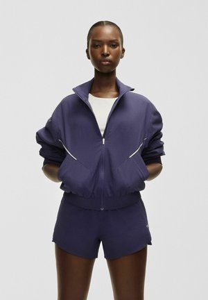 Lila träningsset med en zip-up jacka med texturerad finish och matchande shorts. Båda har elastiska manschetter och en figursydd design.