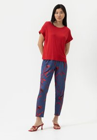 Röd kortärmad topp i kombination med blå byxor med ett rött blommönster. Byxorna har resår i midjan och en avslappnad passform. Röd klacksandaler.