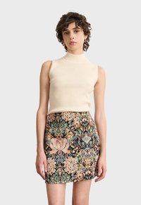 Beiges, geripptes, ärmelloses Top, kombiniert mit einem enganliegenden Minirock mit floralen und barocken Mustern in den Farbtönen Pink, Grün und Schwarz.