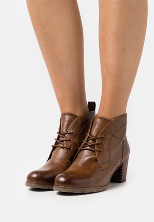 Bottes de cheville en cuir marron avec un bout rond, des lacets et une finition texturée. Elles présentent un talon empilé et des détails de couture sur le côté.