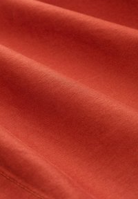 Tkanina boje hrđe s glatkom teksturom, s mekanim nabora i ujednačenim tkanjem. Prikazuje izbliza naglašene detalje materijala.