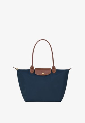Navy blue tote bag made of nylon with brown leather handles and a top flap closure, featuring a gold hardware accent and logo detail.