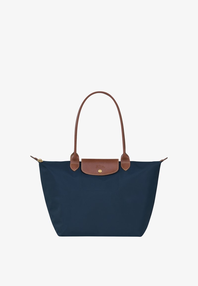 Navy blue tote bag made of nylon with brown leather handles and a top flap closure, featuring a gold hardware accent and logo detail.