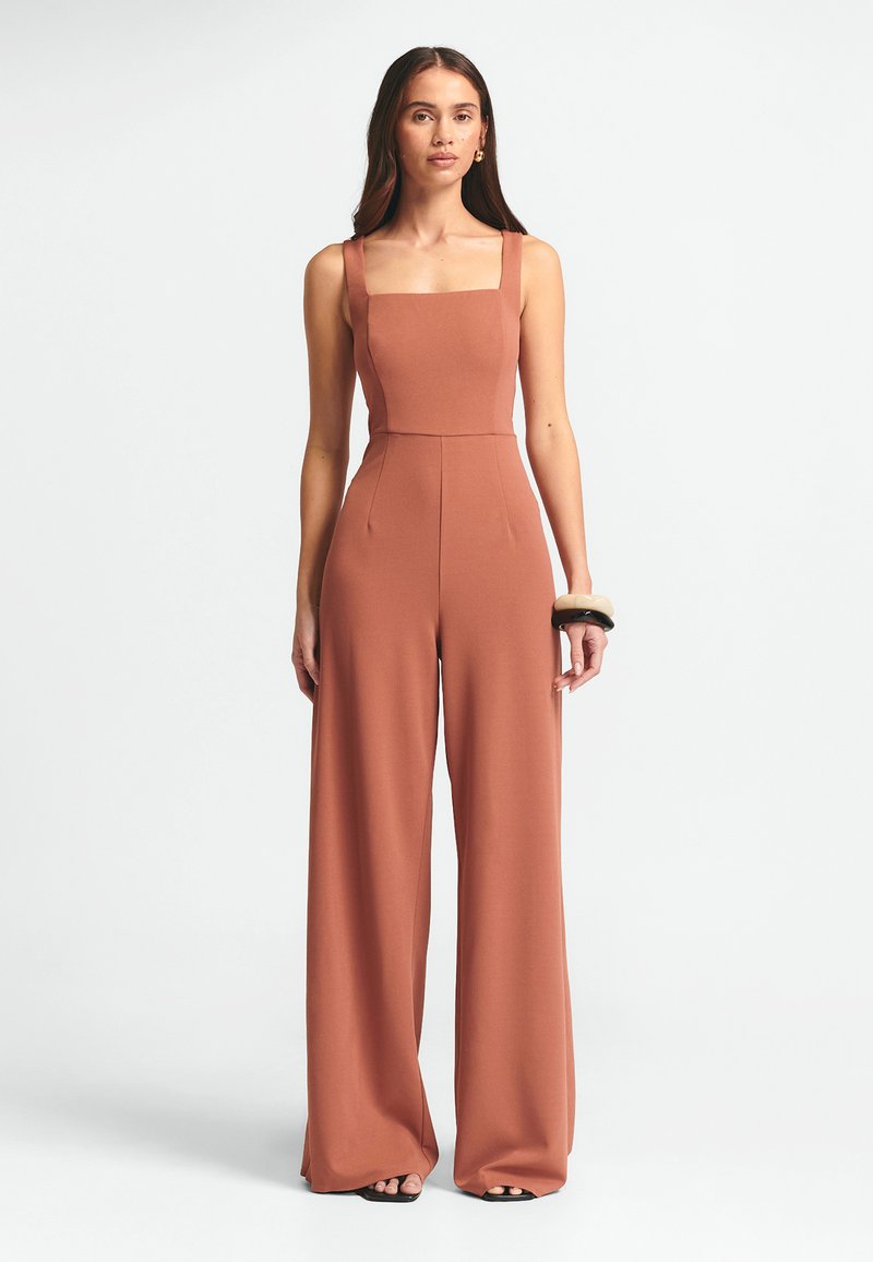 Rostfärgad jumpsuit med fyrkantig halsringning, vida ben och en figurnära överdel. Tillverkad av ett mjukt tyg, med subtila sömmar och sidofickor.