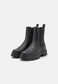 Black Chelsea boots made of smooth leather with elastic side panels, pull tabs, and chunky rubber soles featuring a textured tread pattern.