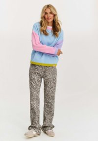 Jasnoniebieski sweter z dzianiny z różowymi i lawendowymi rękawami, w połączeniu z kremowymi i czarnymi spodniami w print w panterkę oraz beżowymi sneakersami.