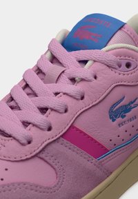 Τα ροζ δερμάτινα αθλητικά παπούτσια διαθέτουν υφασμένο επάνω μέρος, στρογγυλή μύτη και αντιθετικές μπλε και ροζ λεπτομέρειες. Οι κορδόνια είναι υφασμένα, με το λογότυπο στη γλώσσα του παπουτσιού.