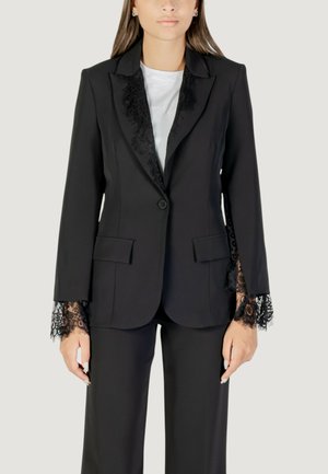 Blazer nero con rifiniture in pizzo sui polsini e sulle rever, caratterizzato da una chiusura a singolo bottone e due tasche frontali, abbinato a pantaloni coordinati.