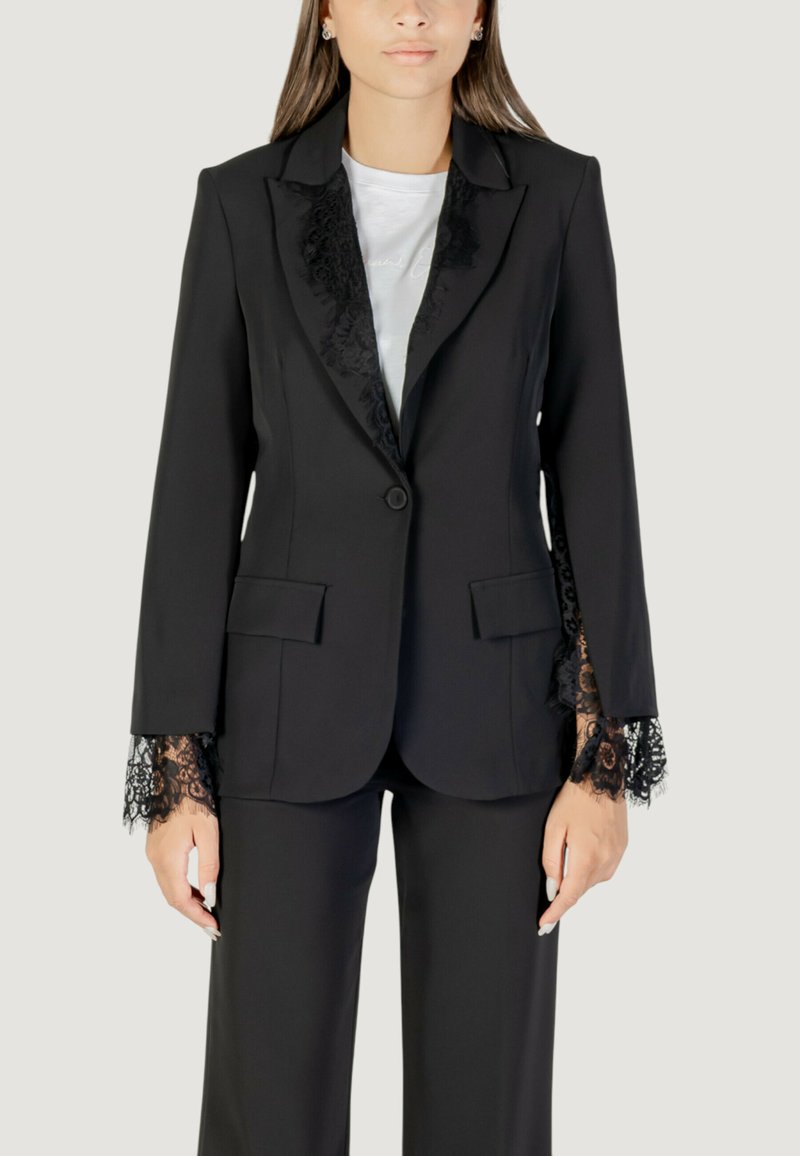 Blazer nero con rifiniture in pizzo sui polsini e sulle rever, caratterizzato da una chiusura a singolo bottone e due tasche frontali, abbinato a pantaloni coordinati.