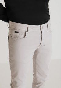 Jeans de mezclilla de color gris claro con corte recto, que cuenta con una cremallera, bolsillos delanteros y un bolsillo trasero con una etiqueta negra.