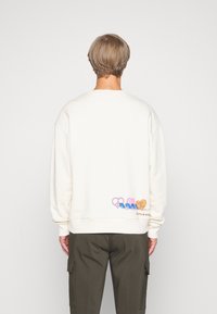 Cremefarbener Sweatshirt mit lockerem Schnitt, mit einem mehrfarbigen Grafikdesign auf der Rückseite, das Liebe und Wellen betont.