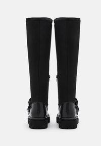 Svarta knähöga stövlar med övre del i slätt tyg, texturerade svarta detaljer, platta sulor och sidodragkedjor för enkel åtkomst.