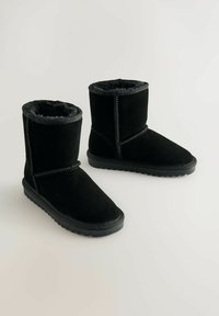 Schwarze Knöchelstiefel aus Wildleder mit einem weichen, Kunstfellfutter. Sie verfügen über eine flache Gummisohle und genähte Details entlang der Nähte.