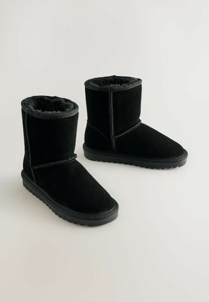 Fekete bokacsizma velúrból, puha műszőrme béléssel. Lapított gumi talppal rendelkezik, és varrott részletek találhatóak az illesztések mentén.