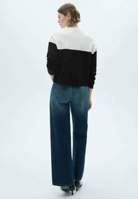 Black and white color-blocked cropped sweater paired with wide-leg blue denim jeans. Model is wearing black high-heeled shoes.