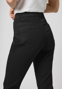 Jeans de mezclilla negra con una silueta ajustada, cintura alta y dos bolsillos traseros con una textura suave. Costuras planas y diseño minimalista.