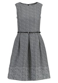 Robe sans manches à pois blancs et noirs, longueur au genou, avec une taille cintrée et une fine ceinture noire.